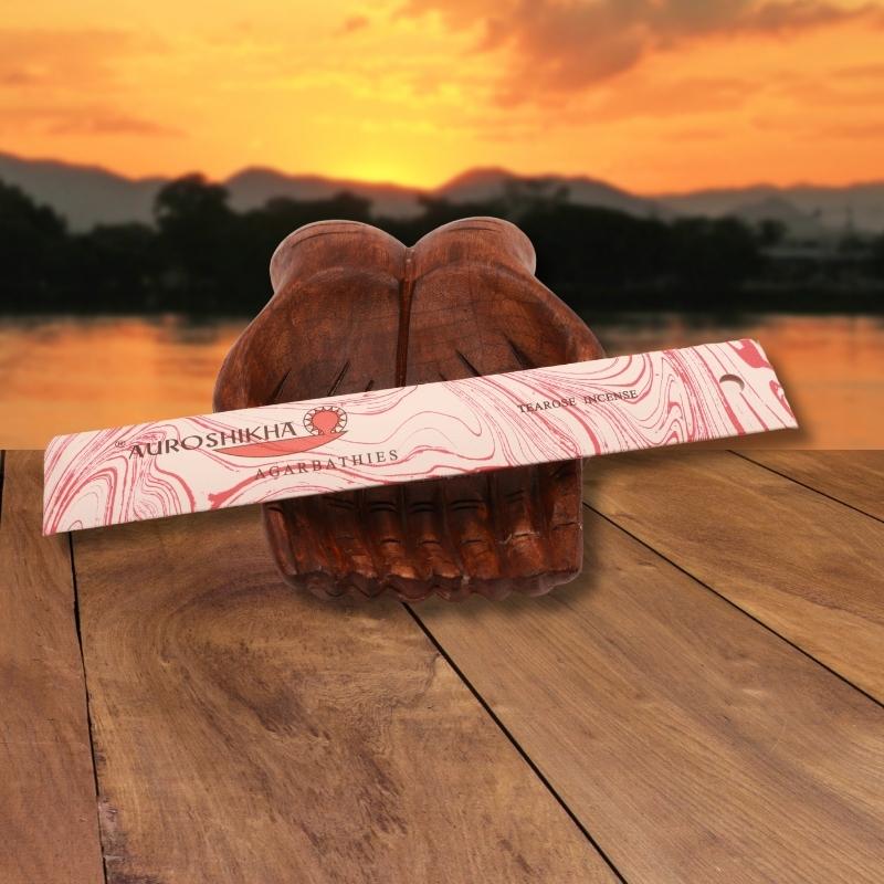 pk of auroshikha incense sitting on a carved wooden hand on a jetty, in front of a golden sunset