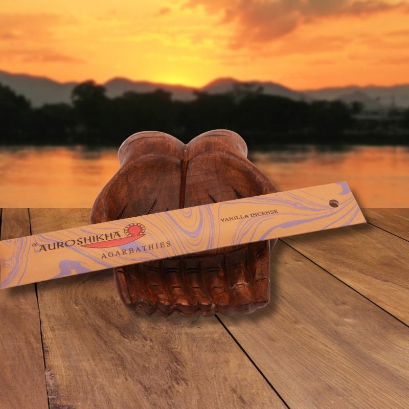 pk of auroshikha incense sitting on a carved wooden hand on a jetty, in front of a golden sunset