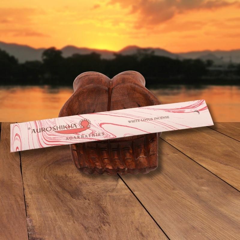 pk of auroshikha incense sitting on a carved wooden hand on a jetty, in front of a golden sunset