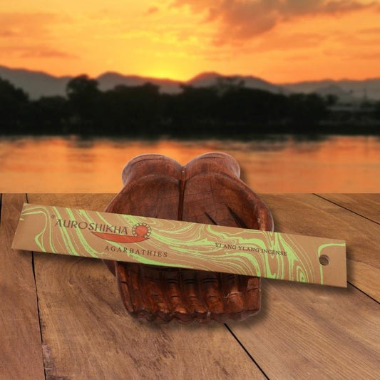 pk of auroshikha incense sitting on a carved wooden hand on a jetty, in front of a golden sunset