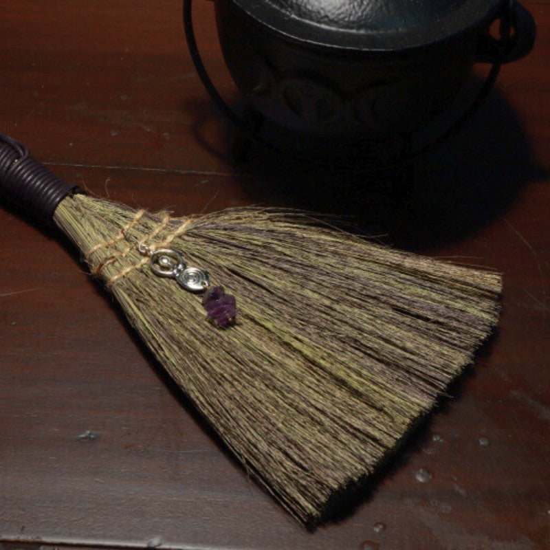 Witches Broom with Amethyst chips and Goddess charm on a wooden table in  front of a cauldron