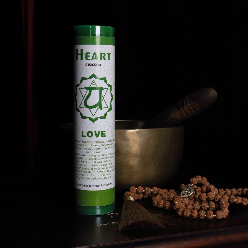 green heart chakra pillar candle in front of a singing bowl with mala beads