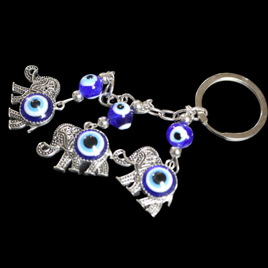 3 silver elephants with a blue and white evil eye bead in the centre of them, attached to a silver chain and ring on a black background