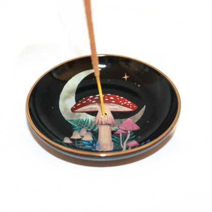 black incense dish with mushrooms, ferns and crescent moon. Stick of incense in the centre hole.