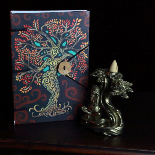 journal with a picture of a tree goddess on the cover, next to a goddess backflow incense cone burner