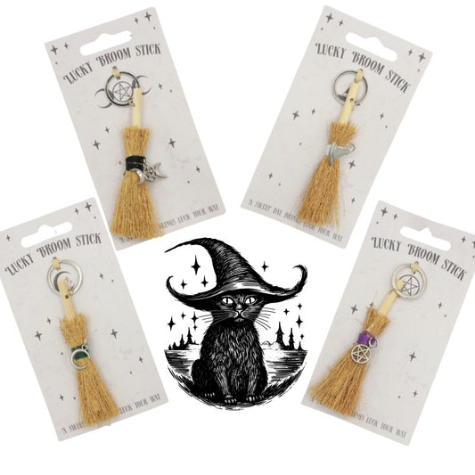 4 keyrings with tiny broomsticks attached. Each with a different silver charm around the handle. Pictured around a black cat that is wearing a witches hat