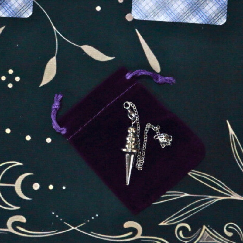 Silver Pendulum on purple velvet bag sitting on a tarot cloth with tarot cards