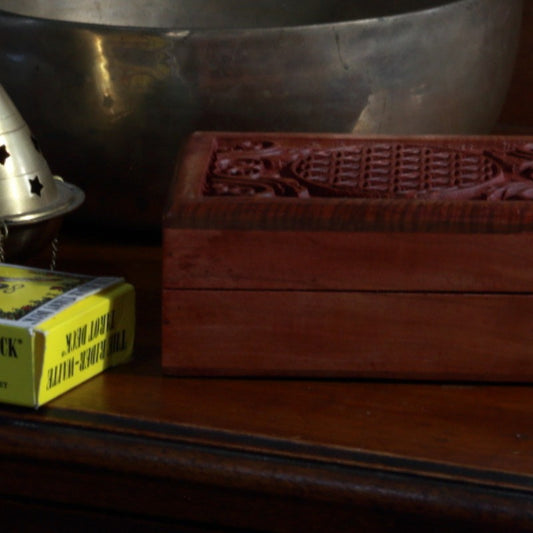 carved wooden box with flower of life design carved on top, sitting in front of brass singing bowl and pack of rider waite smith tarot cards