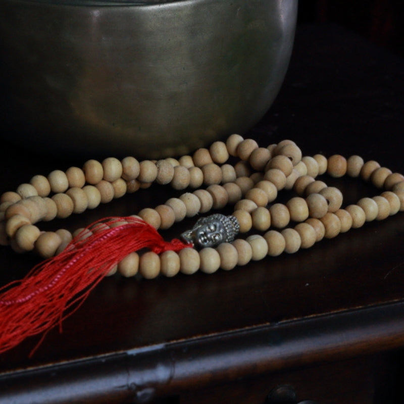 Buddha Head Natural Japa Mala Prayer Beads in front of a singing bowl, on a wooden apothecary cabinet