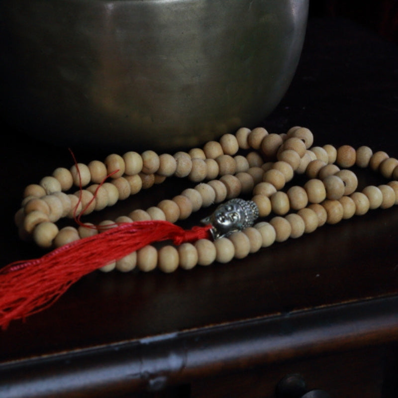 Buddha Head Natural Japa Mala Prayer Beads in front of a singing bowl, on a wooden apothecary cabinet