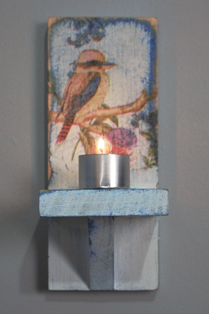 9 hour Metal tealight candle sitting on a distressed blue and white wooden wall mounted candle or ornament shelf decorated with vintage style kookaburra sitting on a branch with red and blue flowers